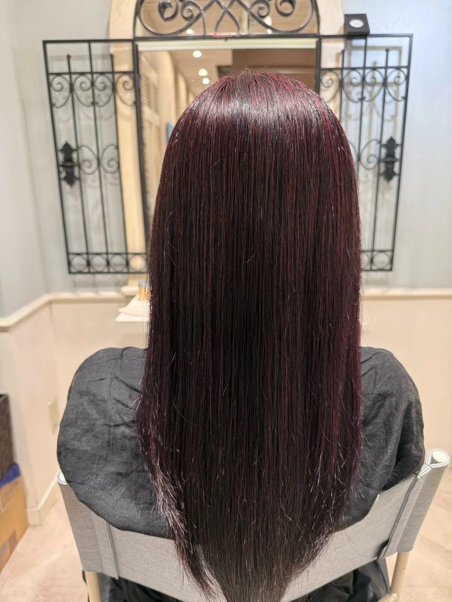 アフター。根元から毛先までまっすぐ整い、面の通った濃い艶のあるワインレッド系のロングヘア。